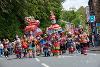 A band of musicians wearing outfits of many brightly coloured ribbons walks down a street as a procession