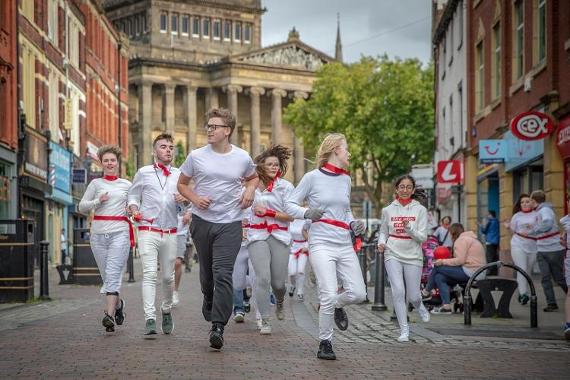 Boys and girls dressed in traditional Spanish bull run clothing, running down Preston's Cheapside.