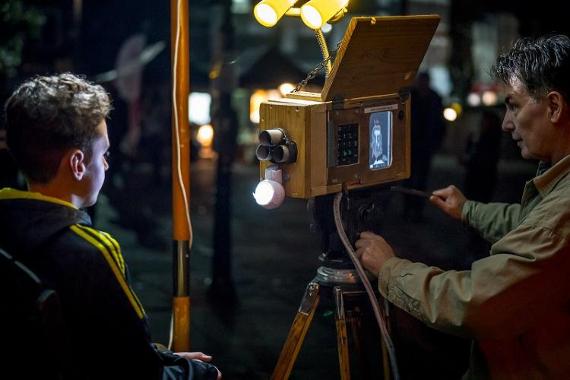 Boy sat down whilst man uses camera to map his face to project on art installment.