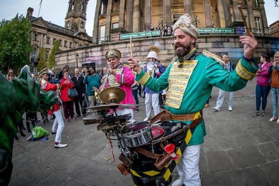 Men dressed in bright band uniforms playing music on Preston Flag Market whilst crowds watch.