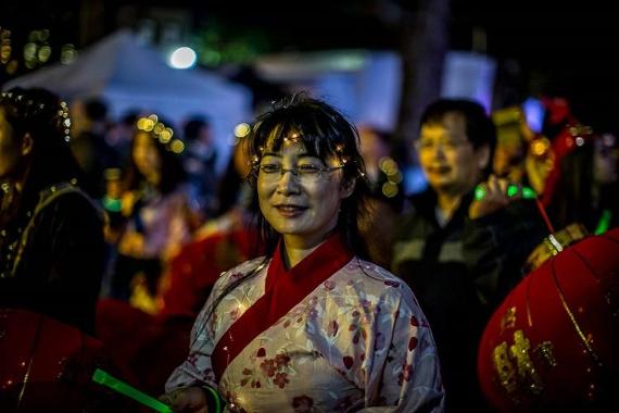 Woman in traditional Chinese robe with lights around her head, taking part in light parade on Preston streets at night.