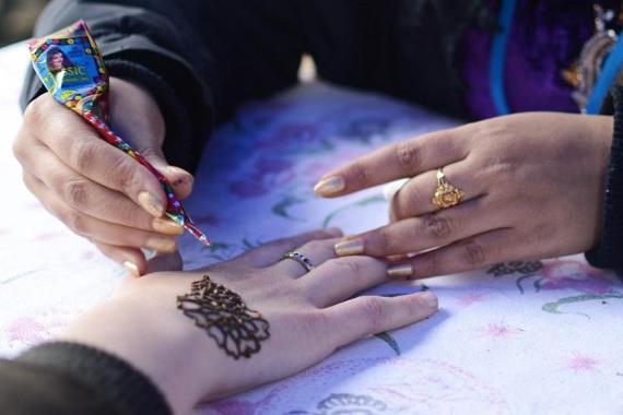 Woman creating a henna tattoo on another woman's hand.