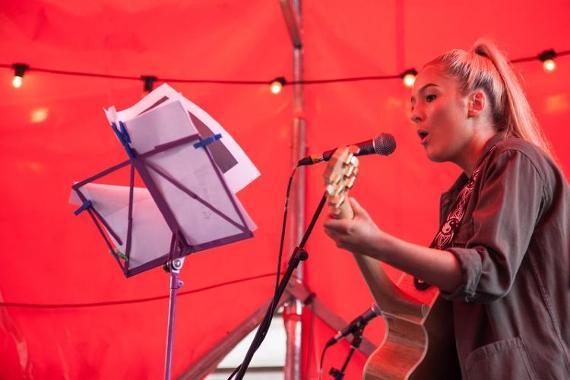Woman singing with guitar inside red tent.