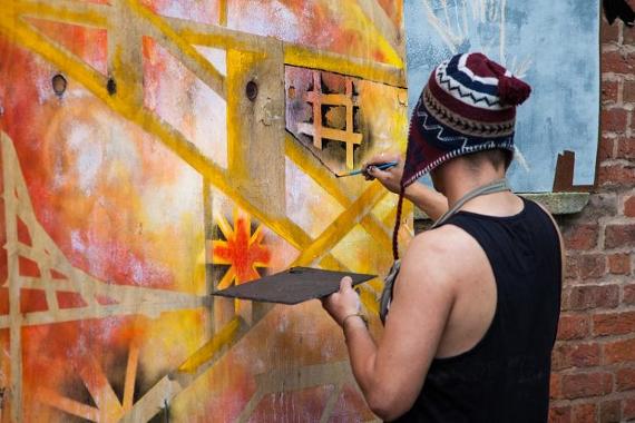 Man painting artwork on large canvas outside on Preston street.