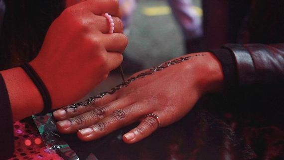Woman decorating another woman's hand with henna tattoo.