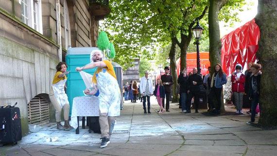 Crowd two street performers dressed as bakers near Preston Flag Market.